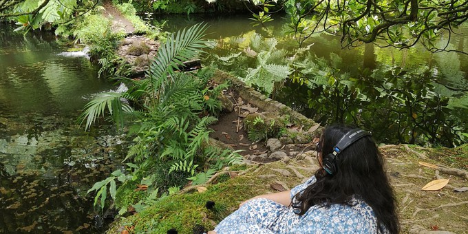 Nikki is wearing headphones and sitting next to a stream or river.