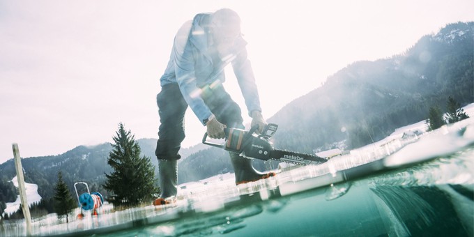 A photo of a person using a chain saw to cut ice out of a frozen lake.